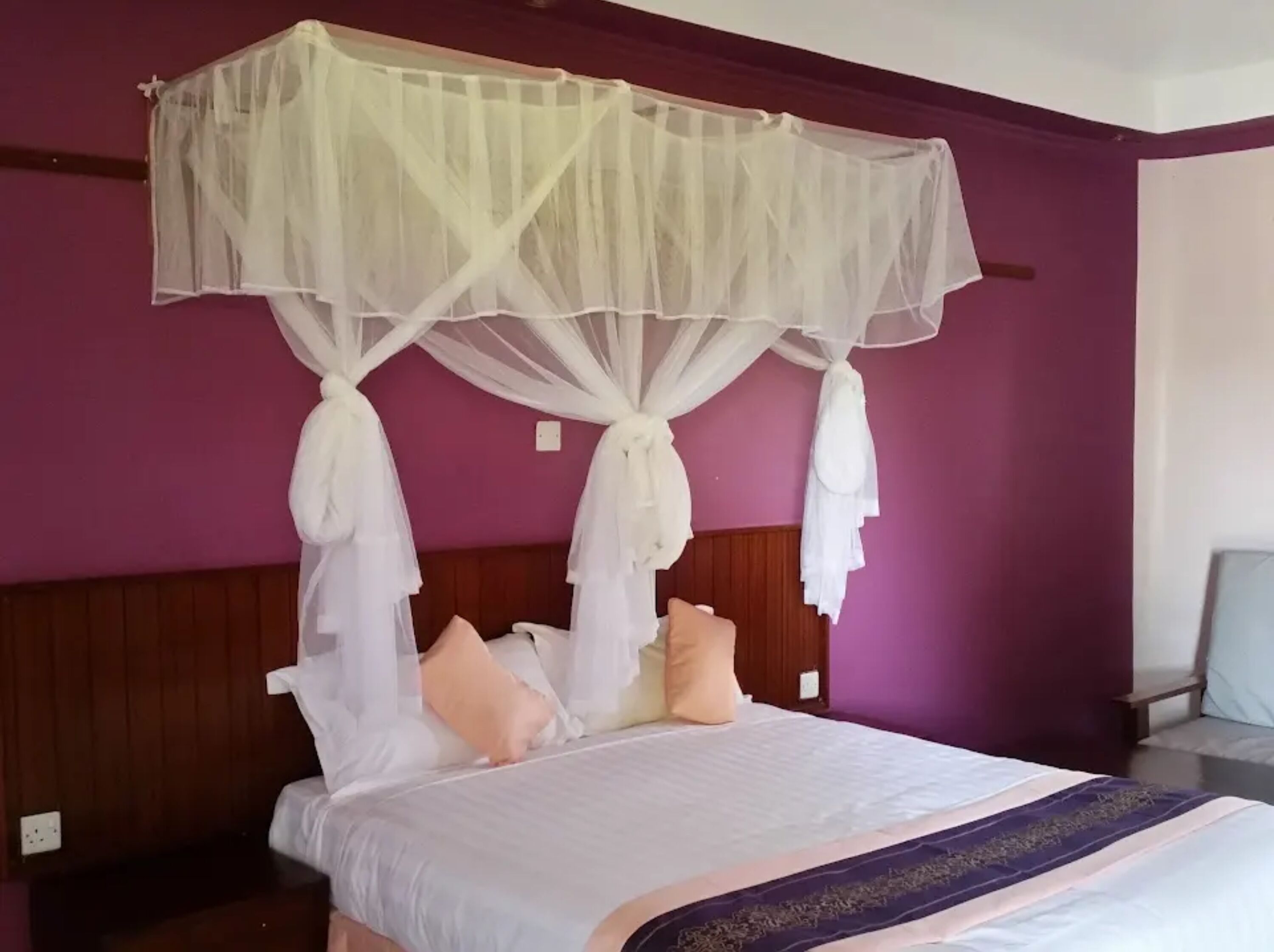 Un lit à baldaquin, une tête de lit en bois et un mur violet.