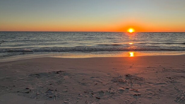 Uma praia ao pôr do sol, com o sol refletindo na água.