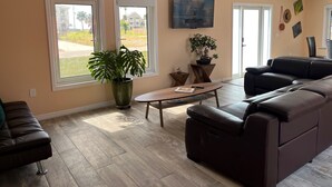 Uma sala de estar com uma janela ampla, um ventilador de teto, uma televisão de tela plana, um sofá, uma mesa de centro e uma planta em vaso.