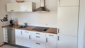 Uma cozinha moderna com armários brancos, exaustor de aço inoxidável, bancada de madeira e lava-louças embutida.