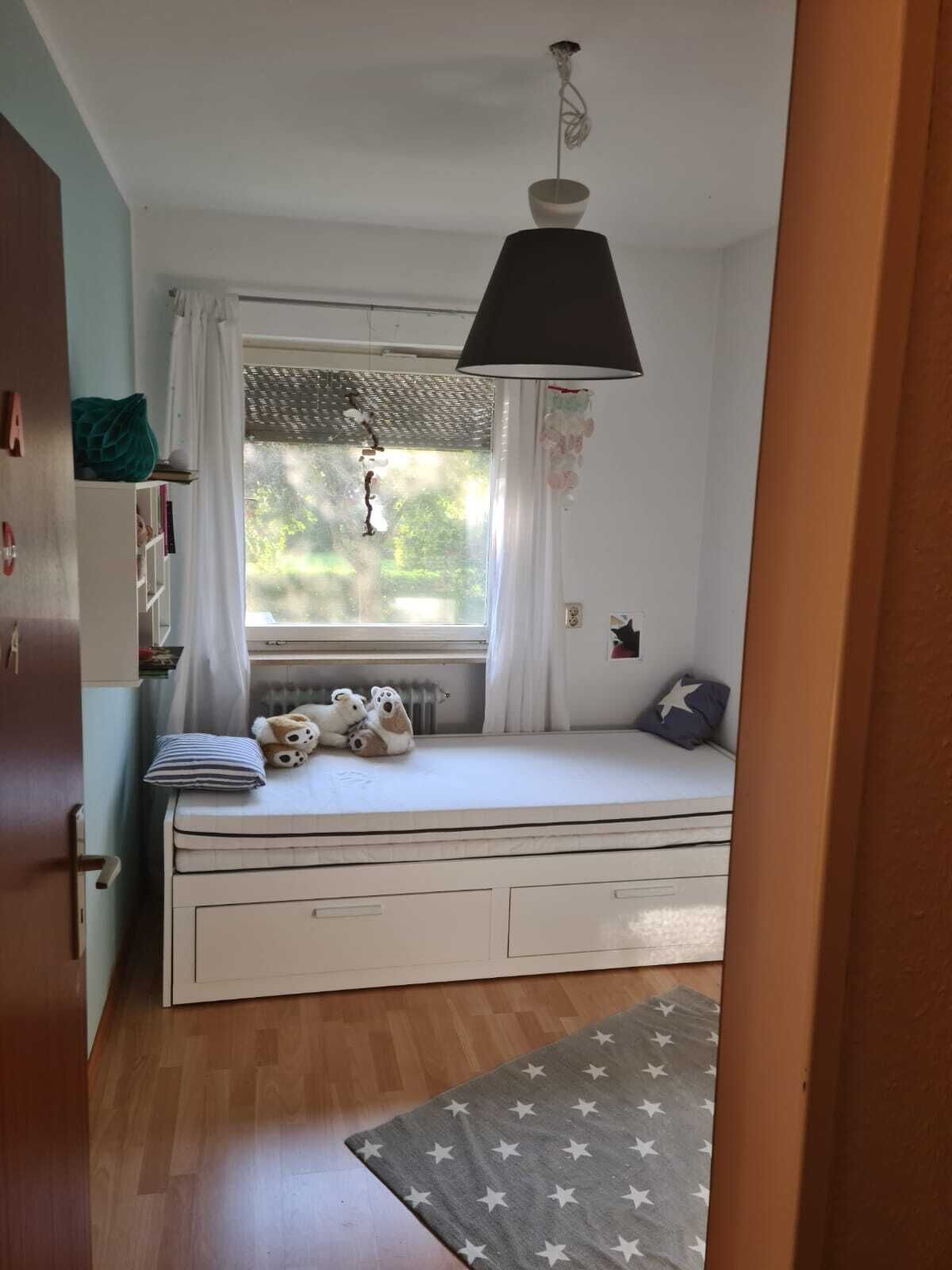 A cozy room with a built-in bed, a window with curtains, a hanging lamp, and a star-patterned rug.