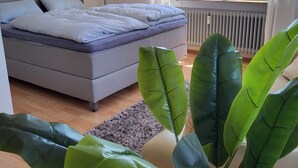 Quarto com cama, radiador, janela com cortinas e vista para um edifício.