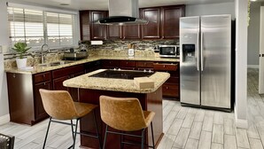 A modern kitchen with dark wood cabinets, stainless steel appliances, granite countertops, and two bar stools. - Cozy, Licensed home, 15min from the strip. (Las Vegas)