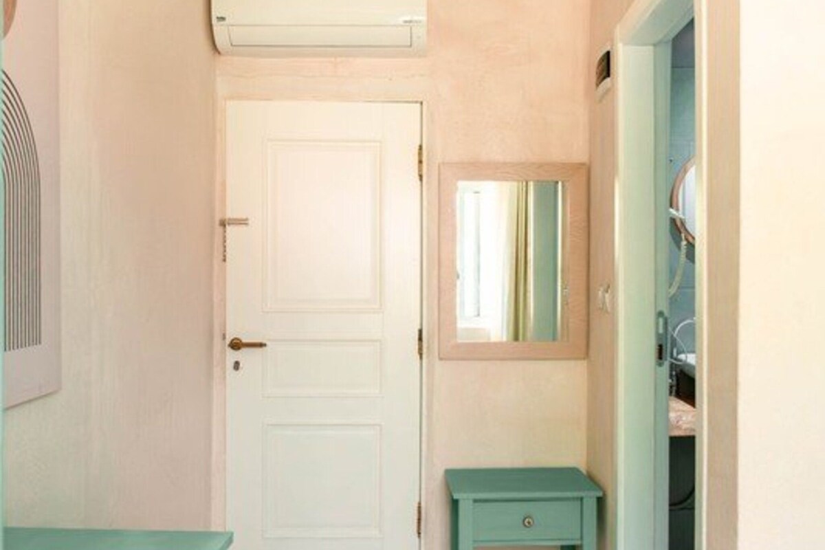 Un pasillo con una puerta blanca, un pequeño banco verde y un espejo en la pared.