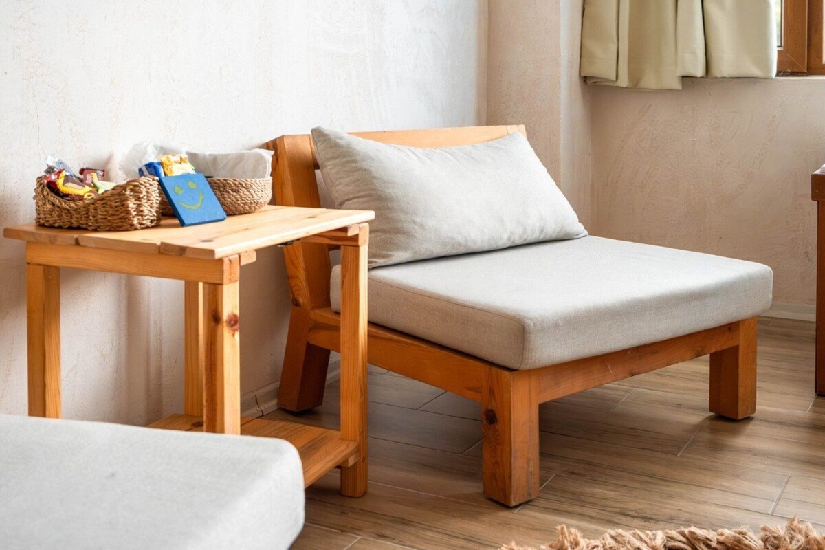 Un banco de madera con cojín, una mesita de madera con cestas y una tarjeta, y una ventana con cortinas.