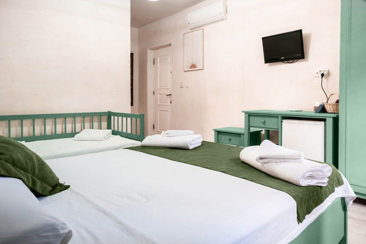 Une chambre d’hôtel avec deux lits, un téléviseur fixé au mur et un petit bureau avec un panier.