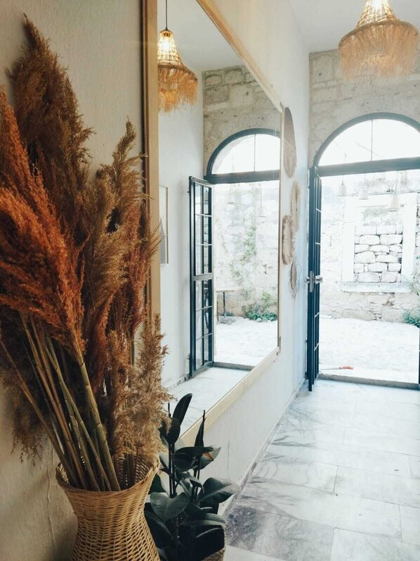A hallway with a large mirror, a wicker basket with dried plants, and a view of an outdoor courtyard.