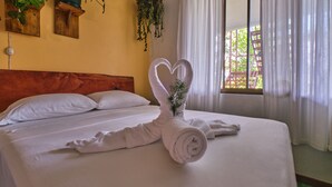 A neatly made bed with a heart-shaped towel arrangement, a wooden headboard, and potted plants on the wall. - Villas Jacquelina (Quepos)