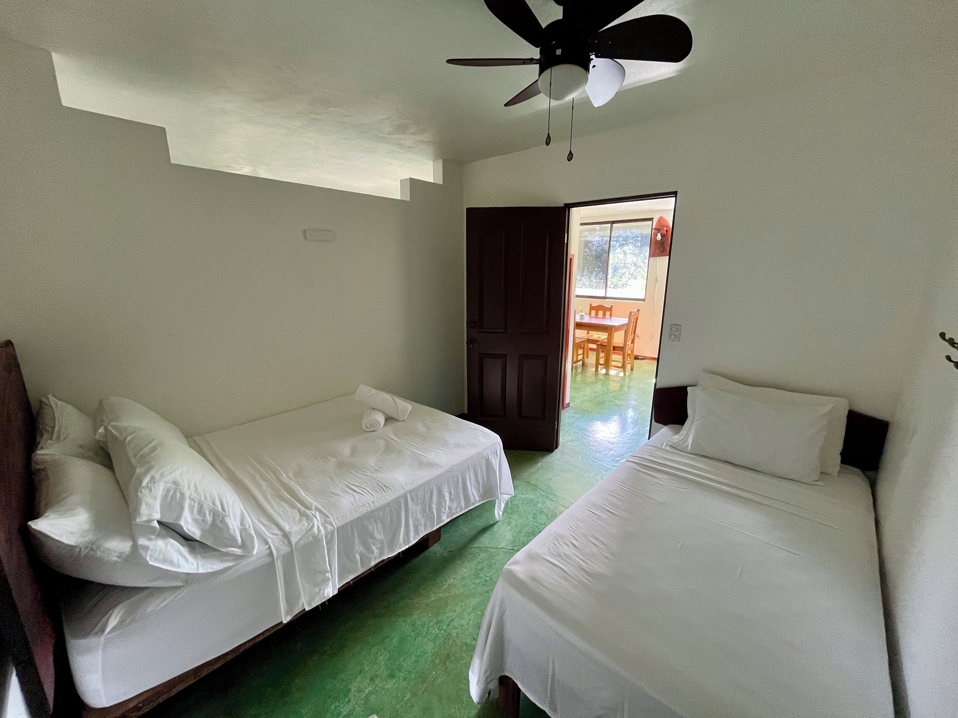 A room with two single beds, a ceiling fan, and a door leading to a balcony with a table and chairs.