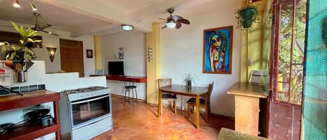Una cocina con estufa a gas, horno y taburetes de bar. Hay una mesa de comedor con sillas y un cuadro en la pared.