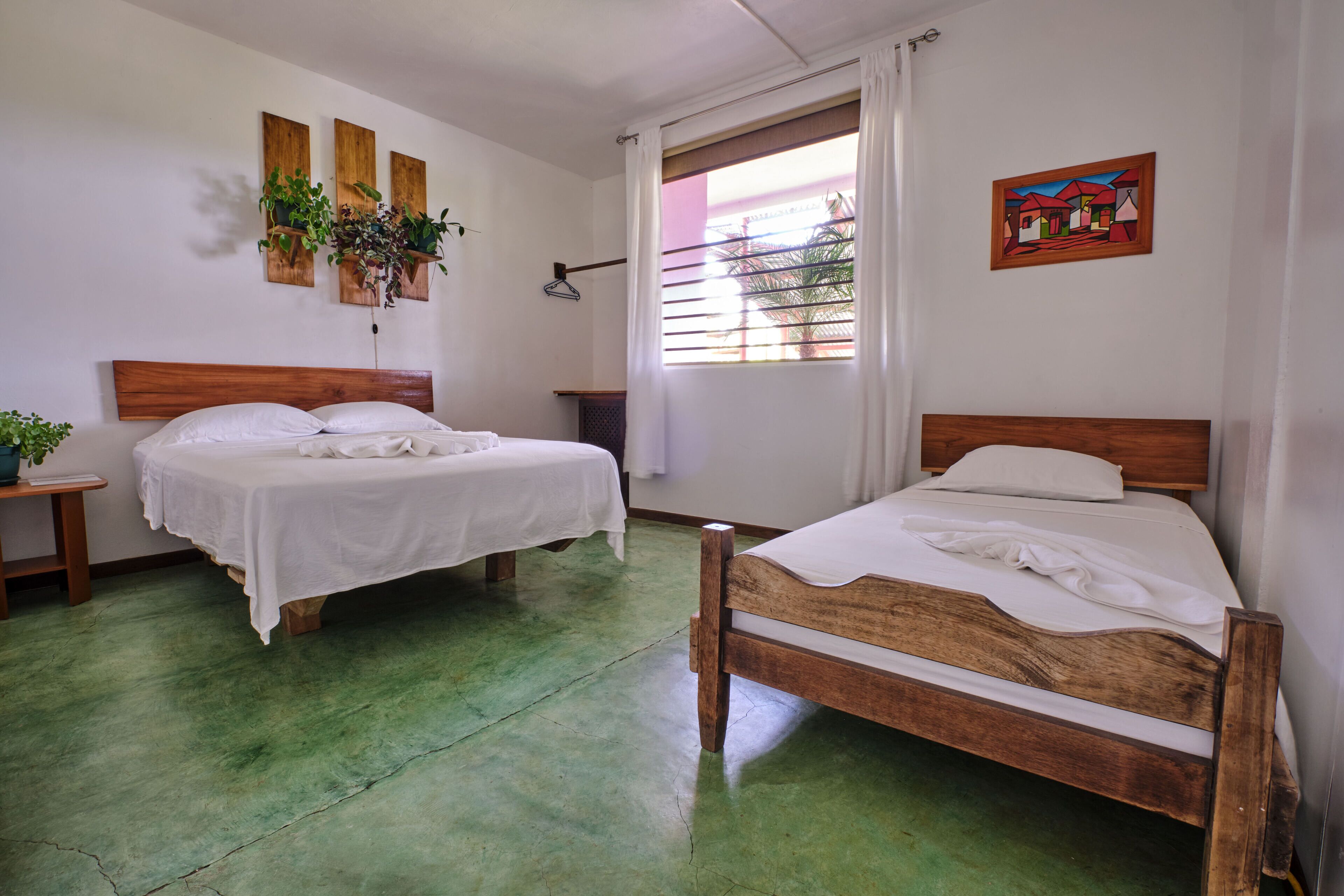 A room with two beds, a wooden headboard, a green floor, a window with curtains, and wall-mounted plants.