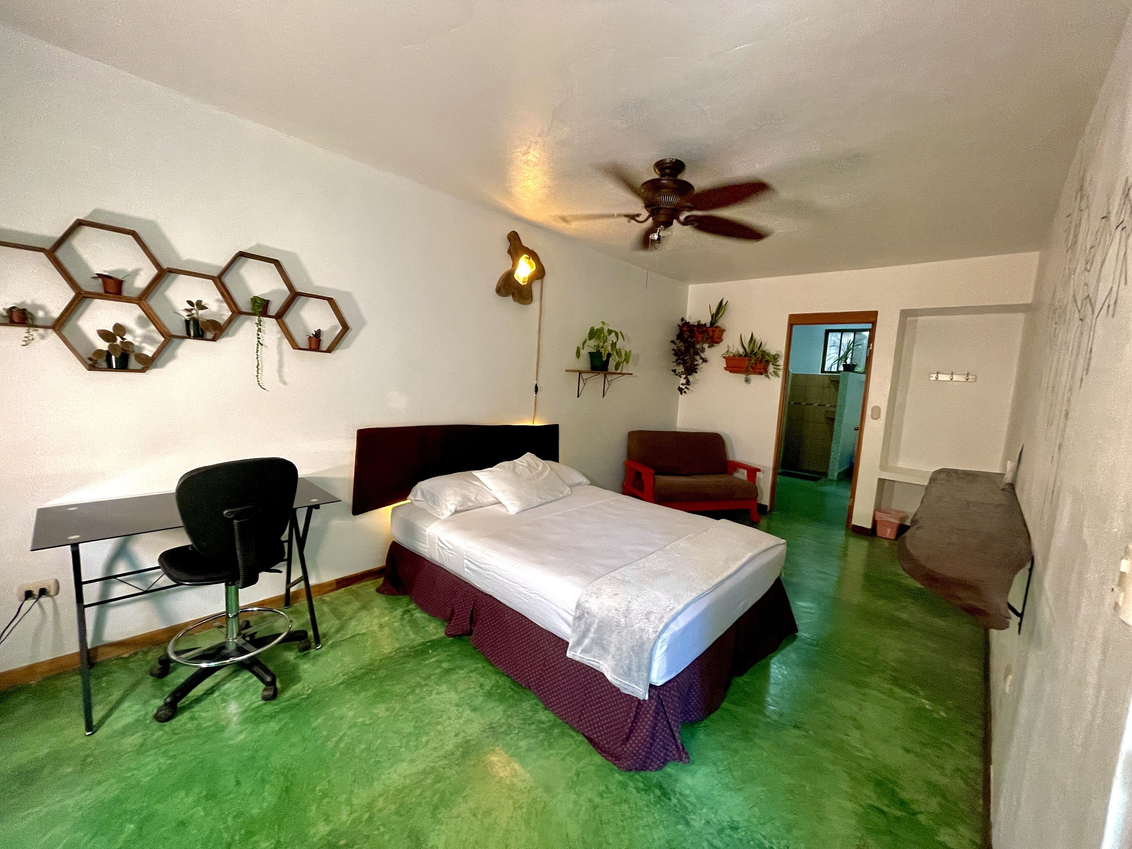 A bedroom with a bed, desk, chair, and a ceiling fan.