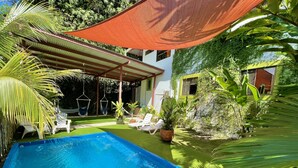 A swimming pool with a covered patio area, surrounded by lush greenery and white lounge chairs. - Villas Jacquelina (Quepos)