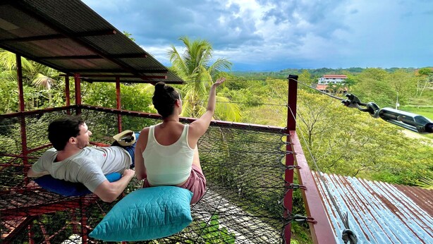 A hammock under a metal roof with a view of a lush landscape and a distant road. - Villas Jacquelina (Quepos)