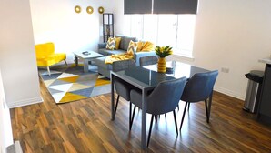 A modern living room with a sofa, coffee table, dining table, and chairs. - Newly refurbished 2 bedroom apartment close to station and local amenities (Hamilton)