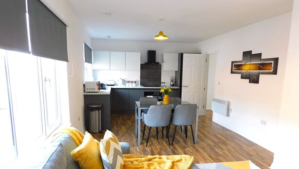 A modern living room with a sofa, a dining area with chairs, a kitchen with cabinets, and a decorative wall piece. - Newly refurbished 2 bedroom apartment close to station and local amenities (Hamilton)