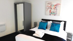A hotel room with a bed, a wardrobe, a painting on the wall, and a bedside table. - Newly refurbished 2 bedroom apartment close to station and local amenities (Hamilton)