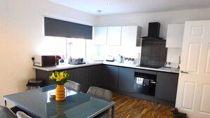 A modern kitchen with a dining area, featuring a glass table, grey chairs, and a central island with a built-in oven. - Newly refurbished 2 bedroom apartment close to station and local amenities (Hamilton)