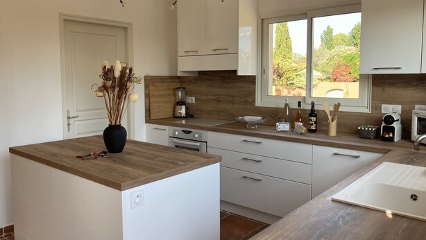 A modern kitchen with white cabinets, a wooden countertop, and a window providing a view of greenery outside.