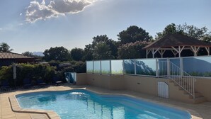 A swimming pool with a curved edge, a covered seating area, and a staircase leading to a covered deck.