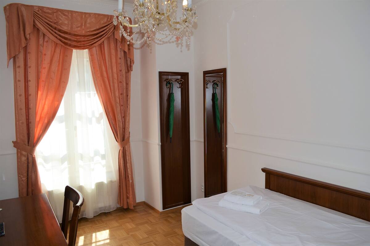 A bedroom with a wooden bed, a wooden chair, a desk, a chandelier, and two doors with green umbrellas.