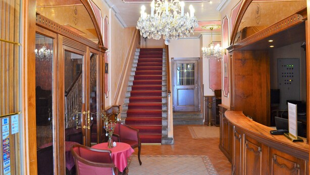 A grand lobby with a marble staircase, a reception desk, and a chandelier. - Renesance Krásná Královna (Karlovy Vary)