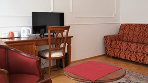 A living room with a wooden desk, a television, a red sofa, and a patterned rug. - Renesance Krásná Královna (Karlovy Vary)