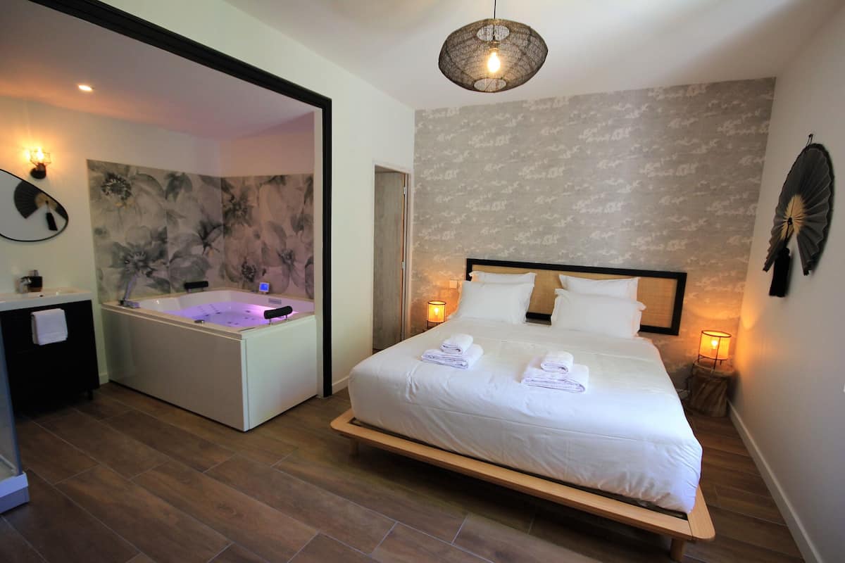 A modern hotel room with a large bed, a separate bathtub, and a wall-mounted fan.