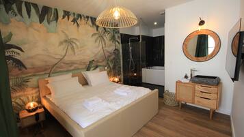 Ein Schlafzimmer mit einem großen Bett, einem Nachttisch aus Holz, einem wandmontierten Spiegel und einem Duschbereich.