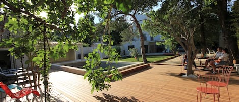 An outdoor wooden deck with seating areas, surrounded by trees and a building in the background.