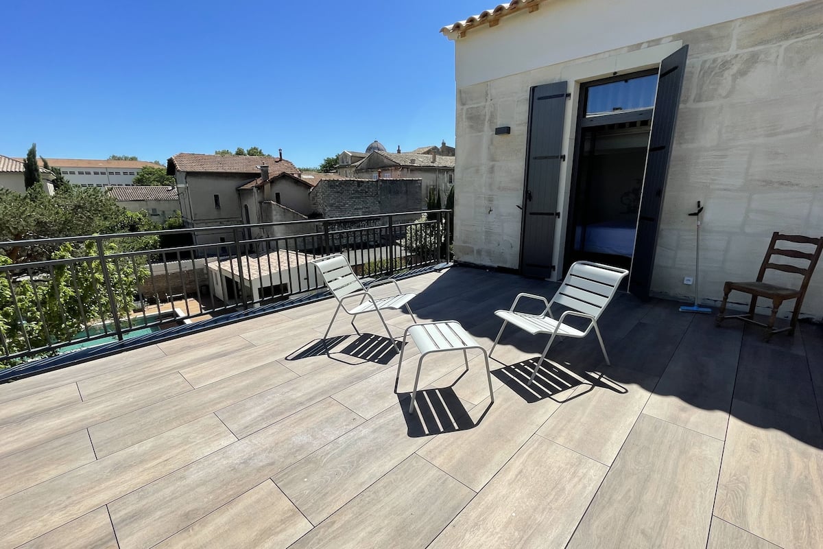 A rooftop terrace with tiled flooring, a metal railing, and two lounge chairs.