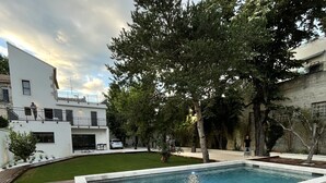 Una piscina con cubierta de madera, rodeada de árboles y un edificio moderno.