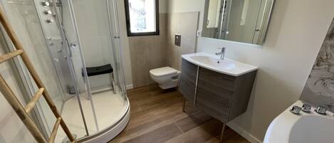 A bathroom with a glass shower enclosure, a toilet, a sink with a mirror, and a bathtub.