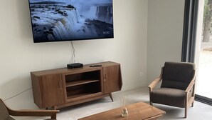 Una sala de estar moderna con un televisor de pantalla plana montado en la pared, muebles de madera y un ventanal con vistas al exterior.