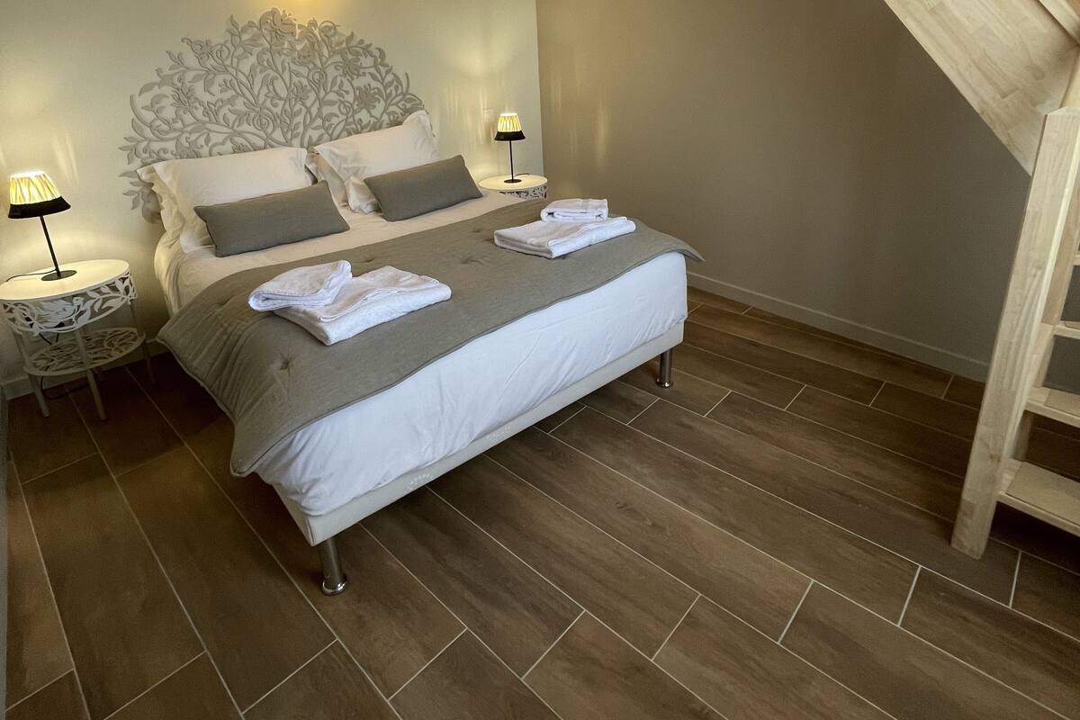 A bedroom with a bed, two bedside tables, a headboard with a light fixture, and a wooden staircase.