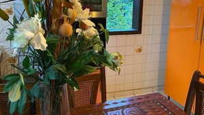 Et spisebord med en vase blomster, en træstol og et køkken med ovn og køleskab.