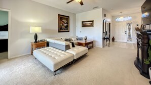Een ruime woonkamer met een grote witte hoekbank, een plafondventilator en een eethoek met een houten tafel en stoelen.