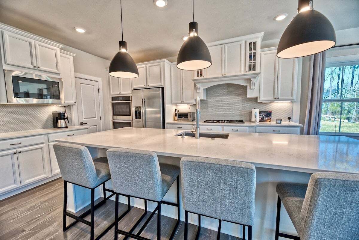 Una cocina moderna con armarios blancos, una isla grande con taburetes de bar e iluminación colgante.