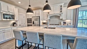 A modern kitchen with white cabinets, a large island with bar stools, and pendant lighting.