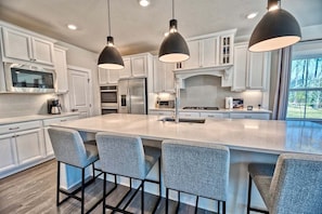 A modern kitchen with white cabinets, a large island with bar stools, and pendant lighting.