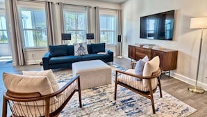 A living room with a sofa, ottoman, chairs, a TV, and a cabinet.
