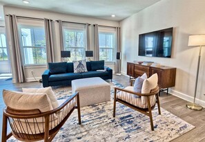 A living room with a sofa, ottoman, chairs, a TV, and a cabinet.