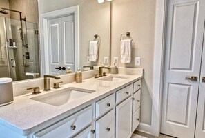 A bathroom with a double sink, a glass shower enclosure, and white cabinetry.