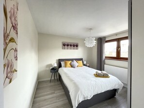 Un dormitorio con cama, mesita de noche, lámpara y ventana con cortinas.