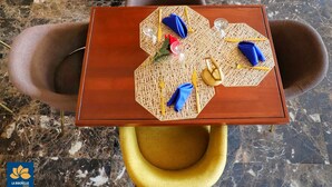 A dining table with a woven placemat, two blue napkins, and a yellow chair. - La Rochelle hôtel (Yaoundé)