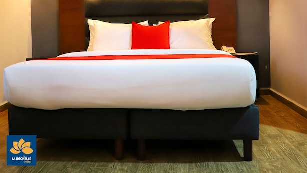 A hotel room with a large bed, a dark headboard, and two wall-mounted lights. - La Rochelle hôtel (Yaoundé)