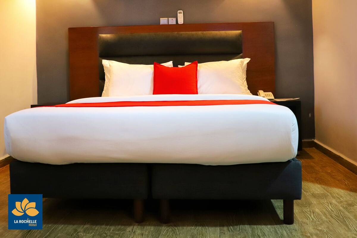 A hotel room with a large bed, a dark headboard, and two wall-mounted lights.