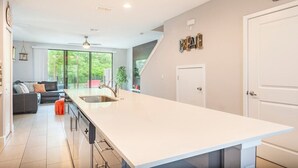 A modern kitchen with a large island, a dining area with a sofa, and a view of greenery outside. - 3BR Resort Pool + Jacuzzi Minutes to Disney 4730 (Kissimmee)
