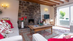 Una sala de estar acogedora con chimenea de piedra, vigas de madera, televisor y vistas al exterior.