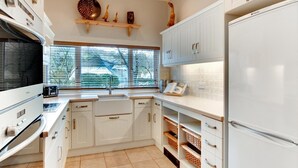 Une cuisine moderne avec des meubles blancs, un four encastré, une grande fenêtre et un plan de travail sur lequel se trouve un grille-pain.